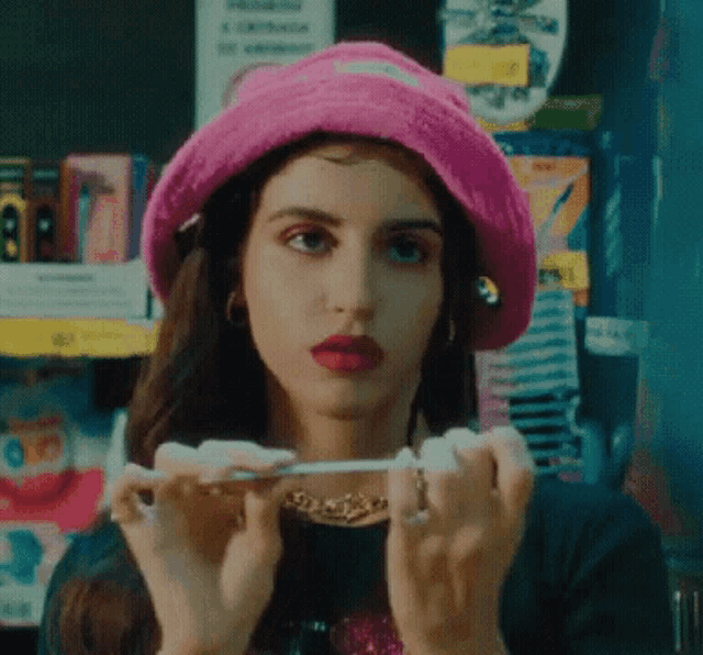 the woman is wearing a pink hat and holding a cigarette in her hands .