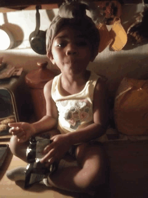a little girl wearing a yellow tank top with a smiley face on it sits on the floor
