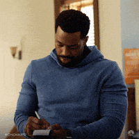 a man in a blue sweater is writing in a notebook