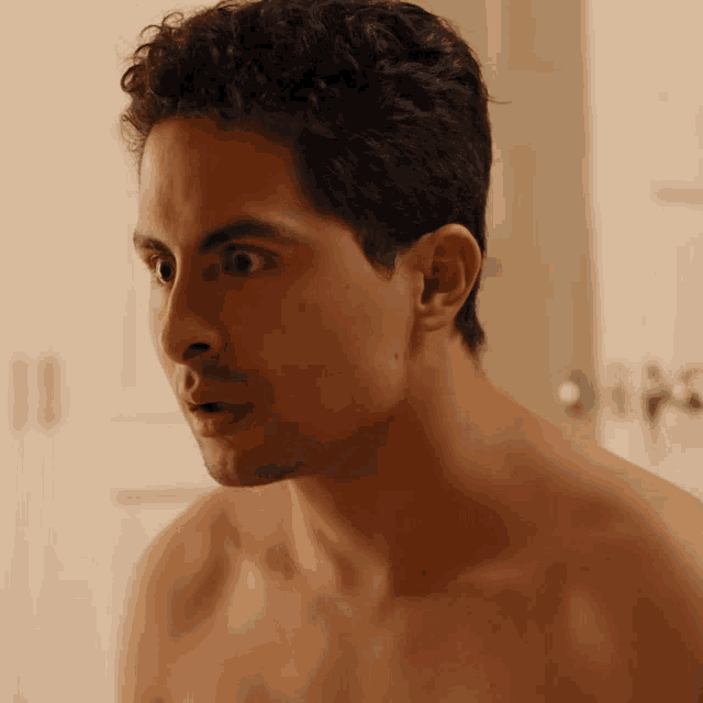 a man without a shirt is looking at himself in a mirror