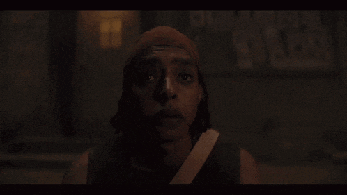 a man wearing a bandana looks at the camera in the dark