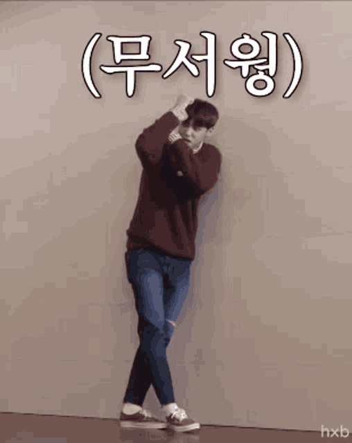 a man in a maroon sweater and jeans is dancing in front of a wall with chinese writing on it