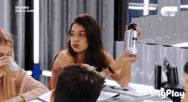 a group of people are sitting around a table and one of them is holding a bottle of water .