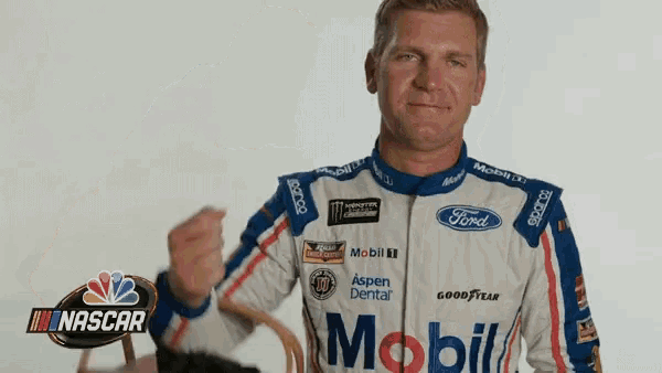 a man in a ford and mobil racing uniform holds his fist up