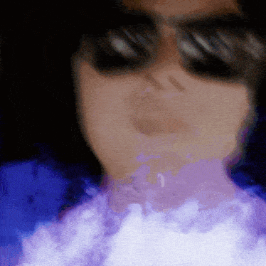 a person wearing sunglasses is blowing purple smoke