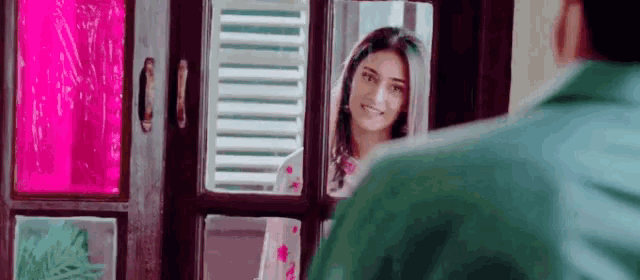 a man is looking at his reflection in a mirror while a woman smiles .