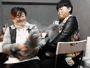 a woman and a child are playing with a cat while sitting in a chair .