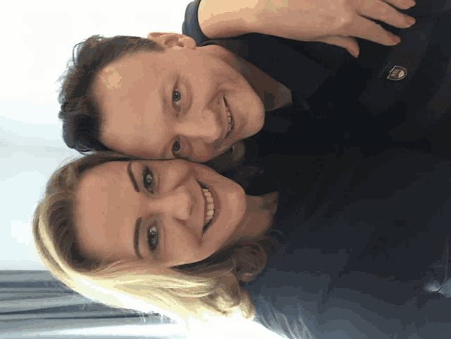 a man and a woman are posing for a picture and the man is wearing a black shirt with a logo on it