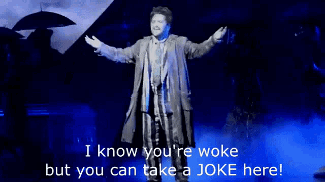 a man stands on a stage with umbrellas and says i know you 're woke but you can take a joke there