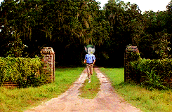 a man in a blue shirt is walking down a dirt road in front of a gate