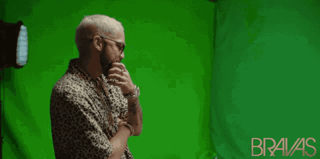 a man in a leopard print shirt stands in front of a green screen that says bravas on it