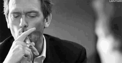 a black and white photo of a man smoking a cigarette and holding his finger to his mouth .