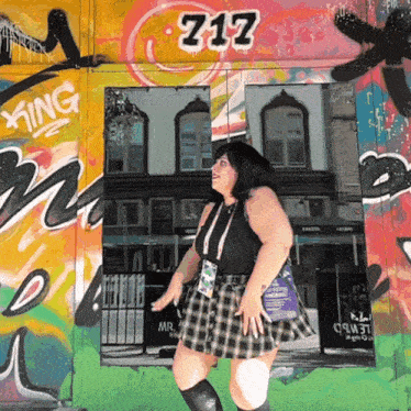 a woman stands in front of a graffiti wall with the number 717 on it