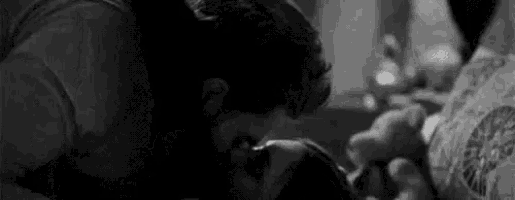 a black and white photo of a man and a woman kissing in bed .