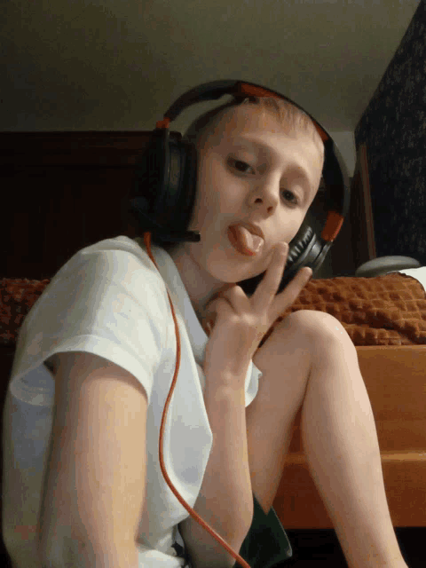 a young boy wearing headphones sticking his tongue out