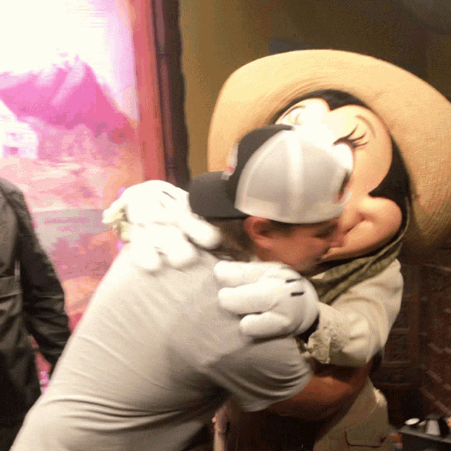 a man hugging a minnie mouse mascot wearing a hat
