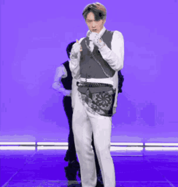 a man wearing a vest and white pants is standing on a stage .