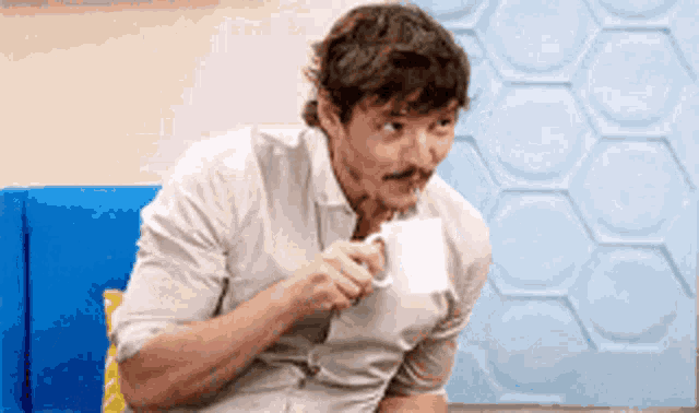 a man with a mustache is drinking a cup of coffee while sitting on a blue couch .