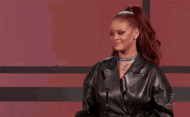 a woman in a leather jacket is standing in front of a microphone and giving a speech .
