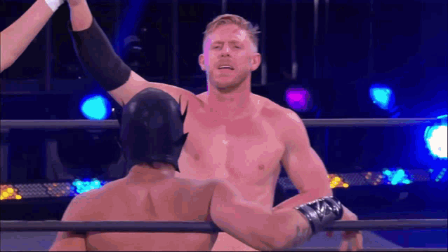a shirtless wrestler in a batman mask is standing next to another wrestler in a wrestling ring .