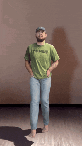 a man wearing a green thrasher t-shirt stands with his hands in his pockets