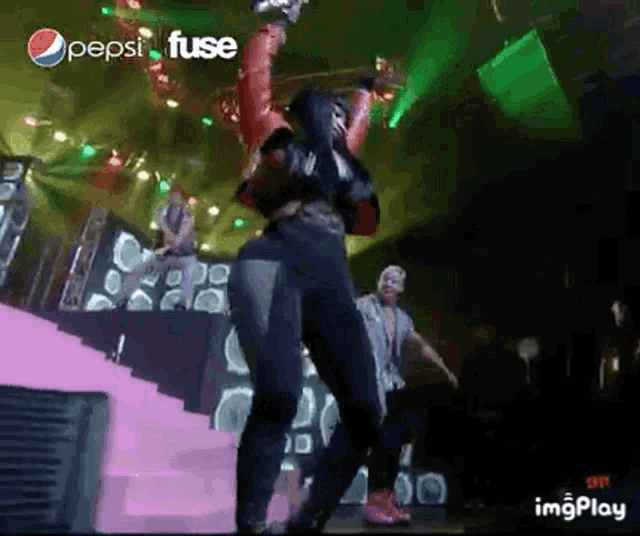 a woman is dancing on a stage with a pepsi fuse ad in the background .