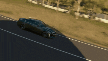 a black car is driving down a road with a grassy hill in the background