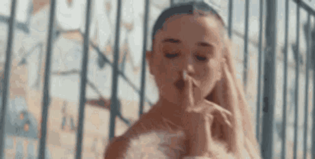 ariana grande is holding her finger to her mouth .