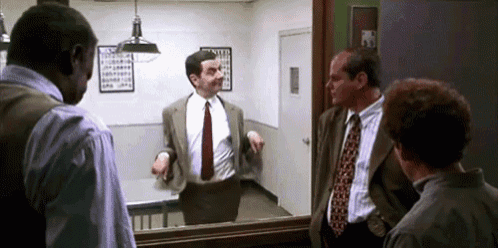 a man in a suit and tie is standing in front of a mirror in a room with other men .