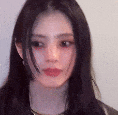 a close up of a woman 's face with long black hair against a white wall .
