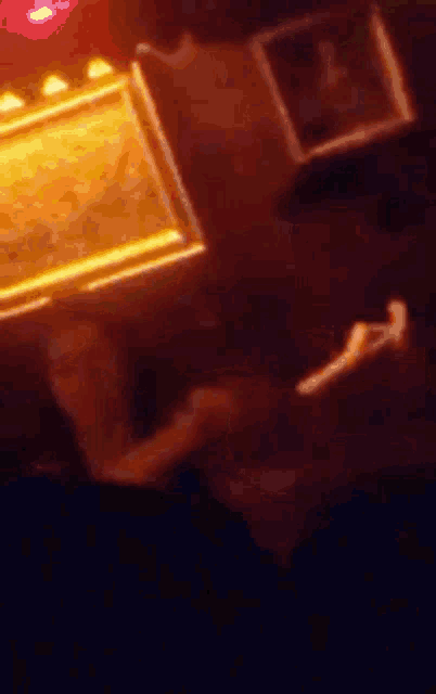 a blurry picture of a person sitting at a table in a dark room with a painting on the wall .