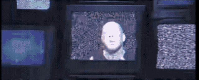 a man 's face is displayed on a television screen surrounded by other television screens