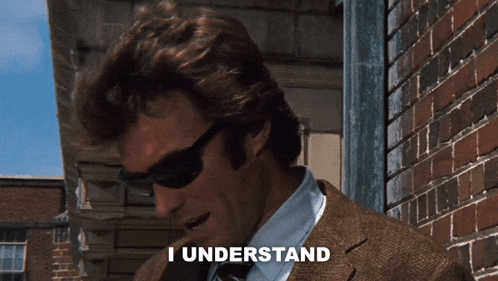 a man wearing sunglasses says i understand in front of a brick building