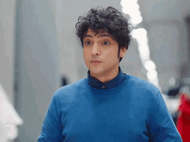 a man with curly hair is wearing a blue sweater and a blue shirt
