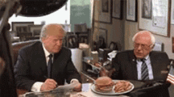 two men are sitting at a table with hamburgers and french fries .