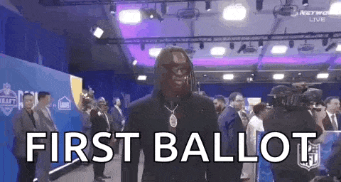 a man with a mask on his face is standing in a room with the words `` first ballot '' written on the wall .