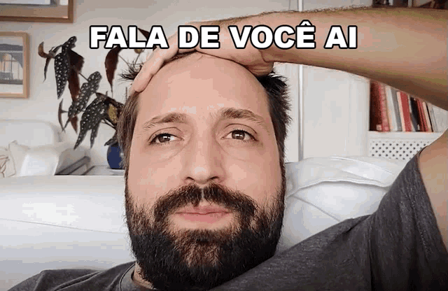 a man with a beard holds his hand to his forehead with the caption fala de voce ai above him