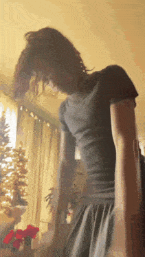 a woman in a black shirt is standing in a room with a christmas tree in the background
