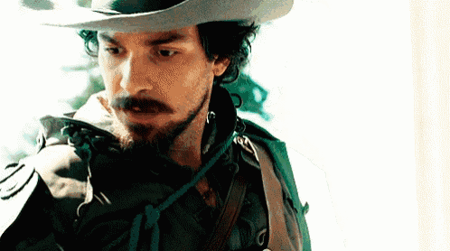a man with a beard is wearing a cowboy hat and a sword .