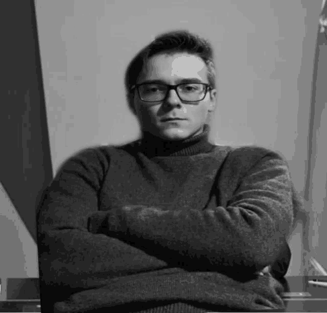 a man wearing glasses and a sweater is sitting with his arms crossed .
