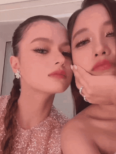 two women are posing for a picture together and one of them is touching her face .