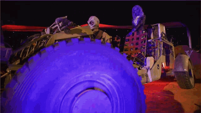 a man in a mask stands in front of a giant tire that says ' us army ' on it