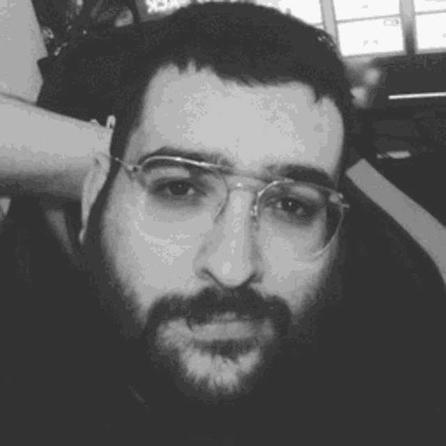 a man with glasses and a beard is looking at the camera in a black and white photo