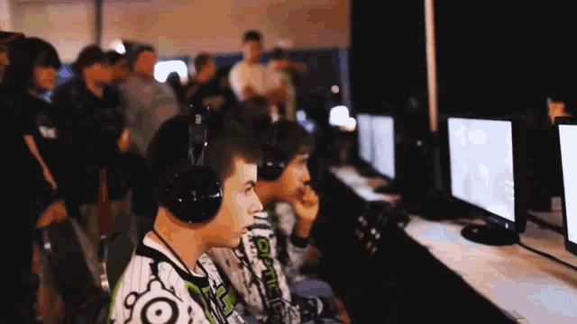 two boys wearing headphones are playing a video game and one of them has the word optic on his shirt
