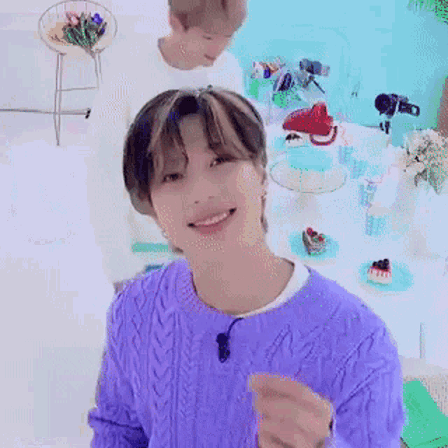 a young man in a purple sweater is smiling while sitting at a table with cakes .