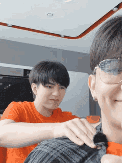 a man wearing glasses and an orange shirt is putting something on another man 's back