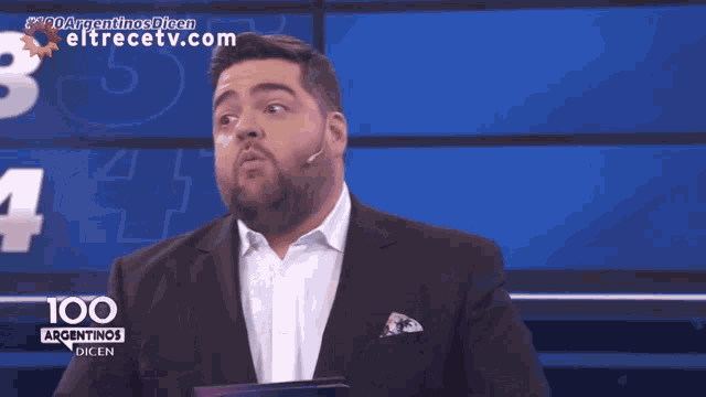 a man in a suit stands in front of a screen that says 100 argentinas