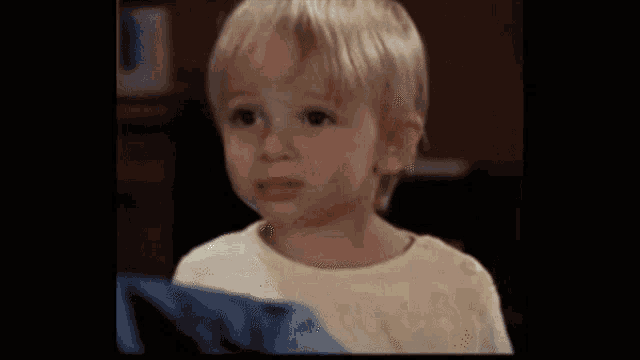 a little boy in a yellow shirt is making a funny face and looking at the camera .