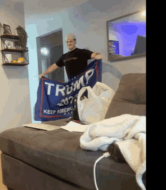 a man in a black shirt holds up a blue flag that says trump