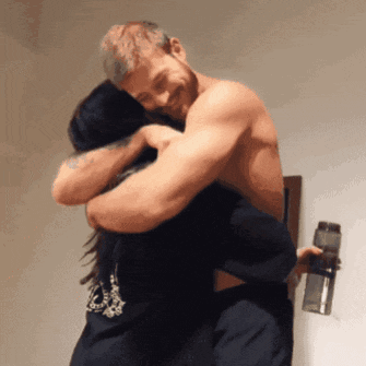 a man without a shirt is hugging a woman who is wearing a shirt that says ' a ' on it